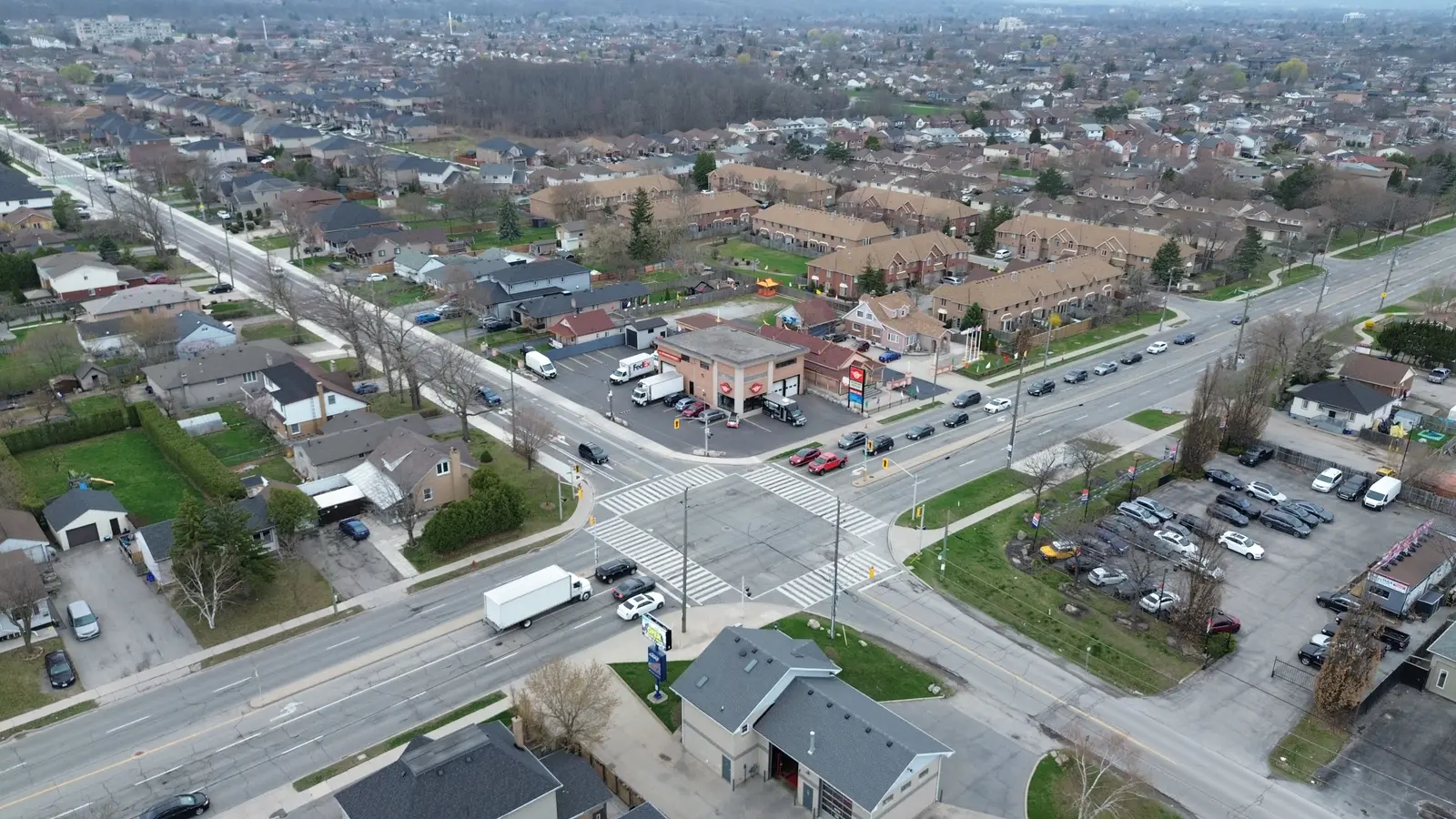 Aerial view of a signalized suburban intersection with a two-storey masonry commercial building on the corner lot, residential streets behind