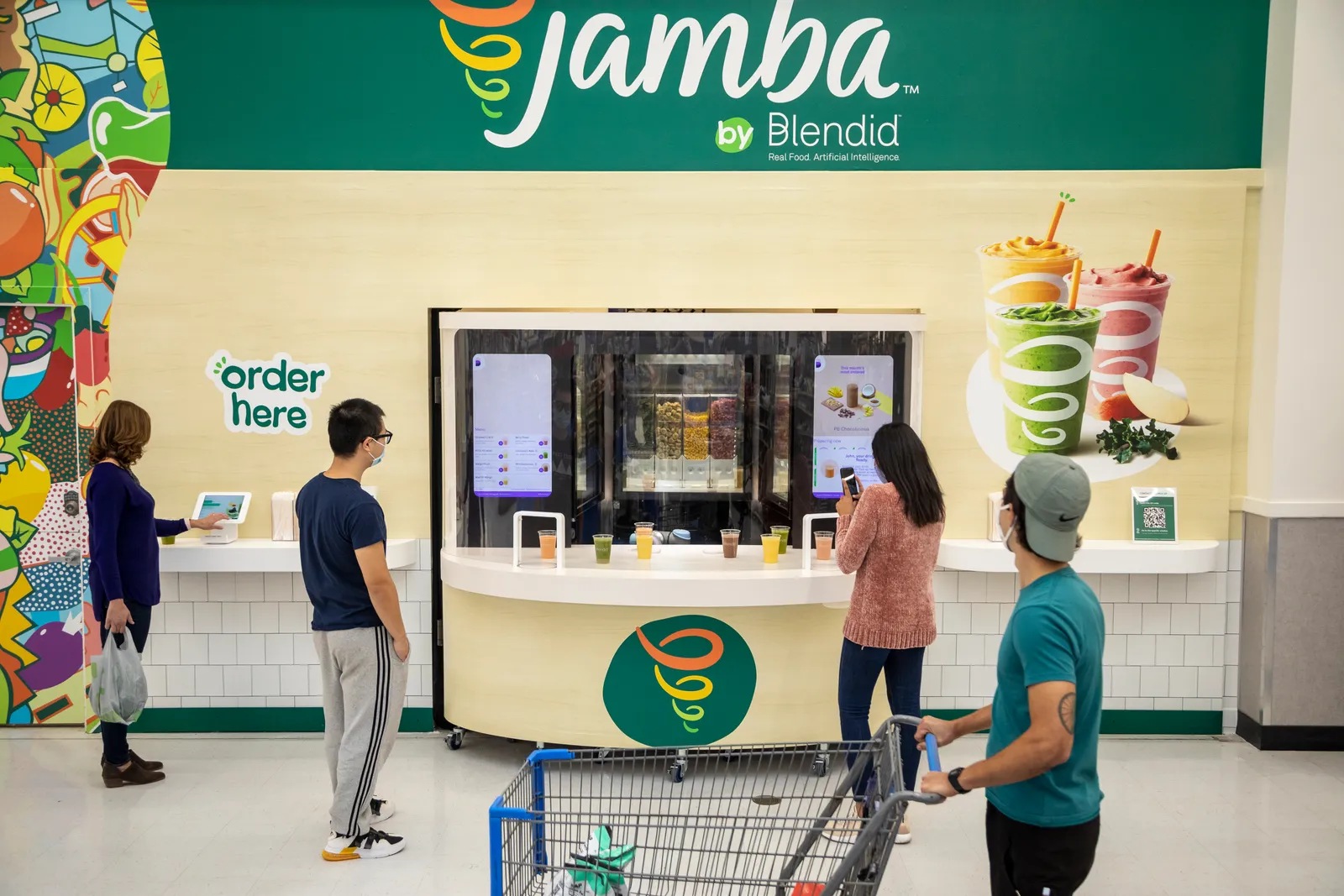 Shoppers order at the Jamba by Blendid robotic smoothie kiosk inside a Walmart, the robot arm working behind glass