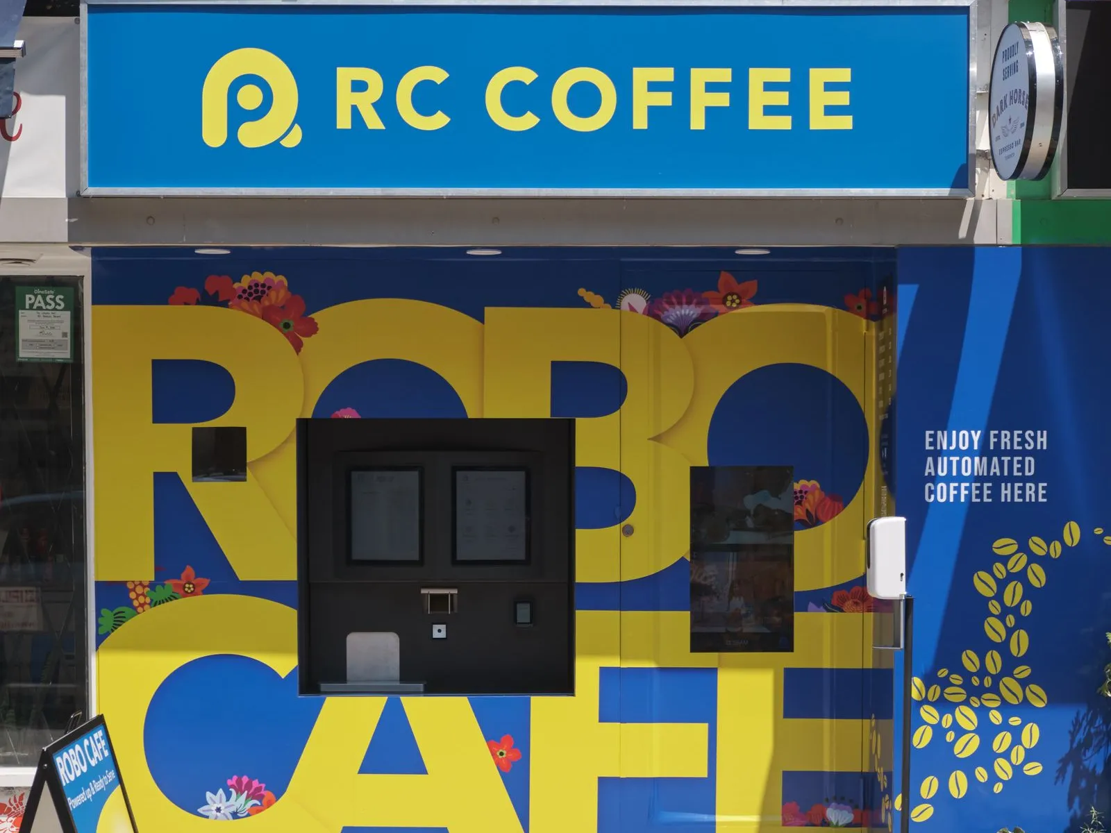 RC Coffee Robo Cafe storefront on a Toronto sidewalk, an automated espresso kiosk set into a blue and yellow wall