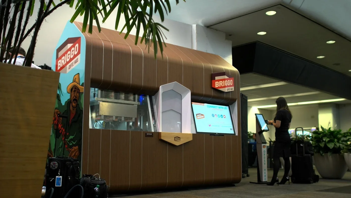 Briggo Coffee Haus kiosk in an airport terminal with a traveller ordering at a screen