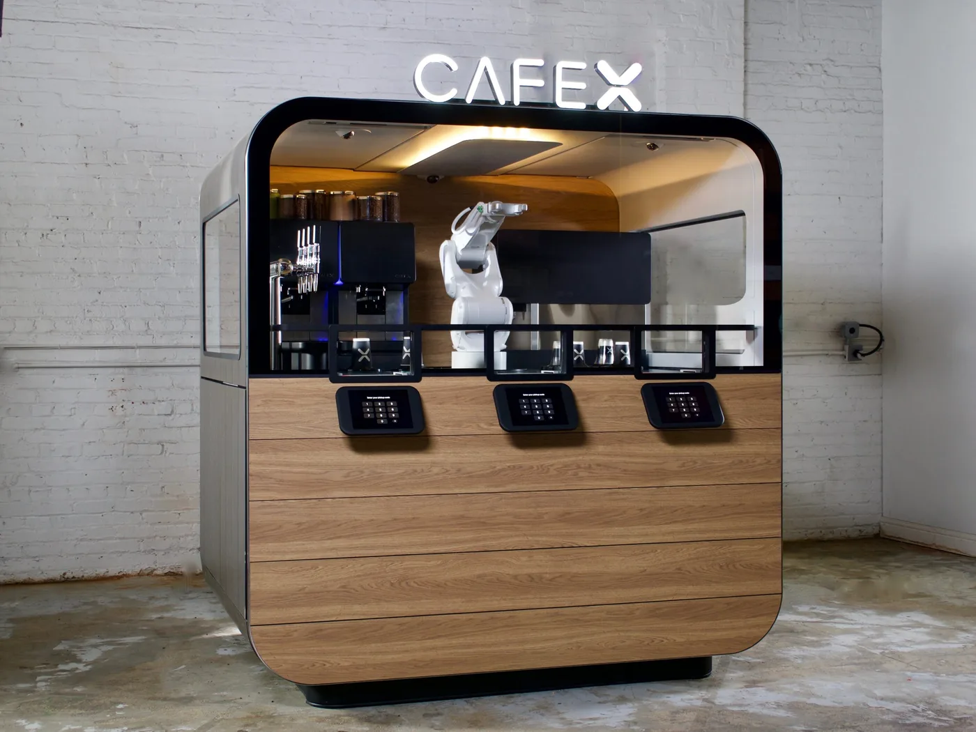 Cafe X kiosk with a white robot arm behind glass and three ordering tablets