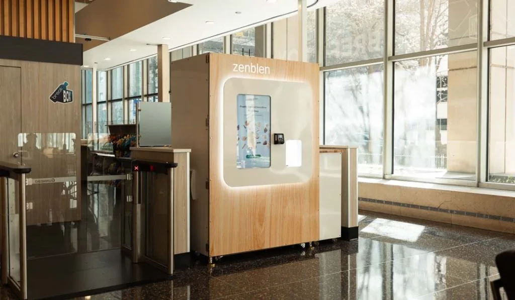 Zenblen robotic smoothie kiosk in a glass-walled building lobby next to security turnstiles