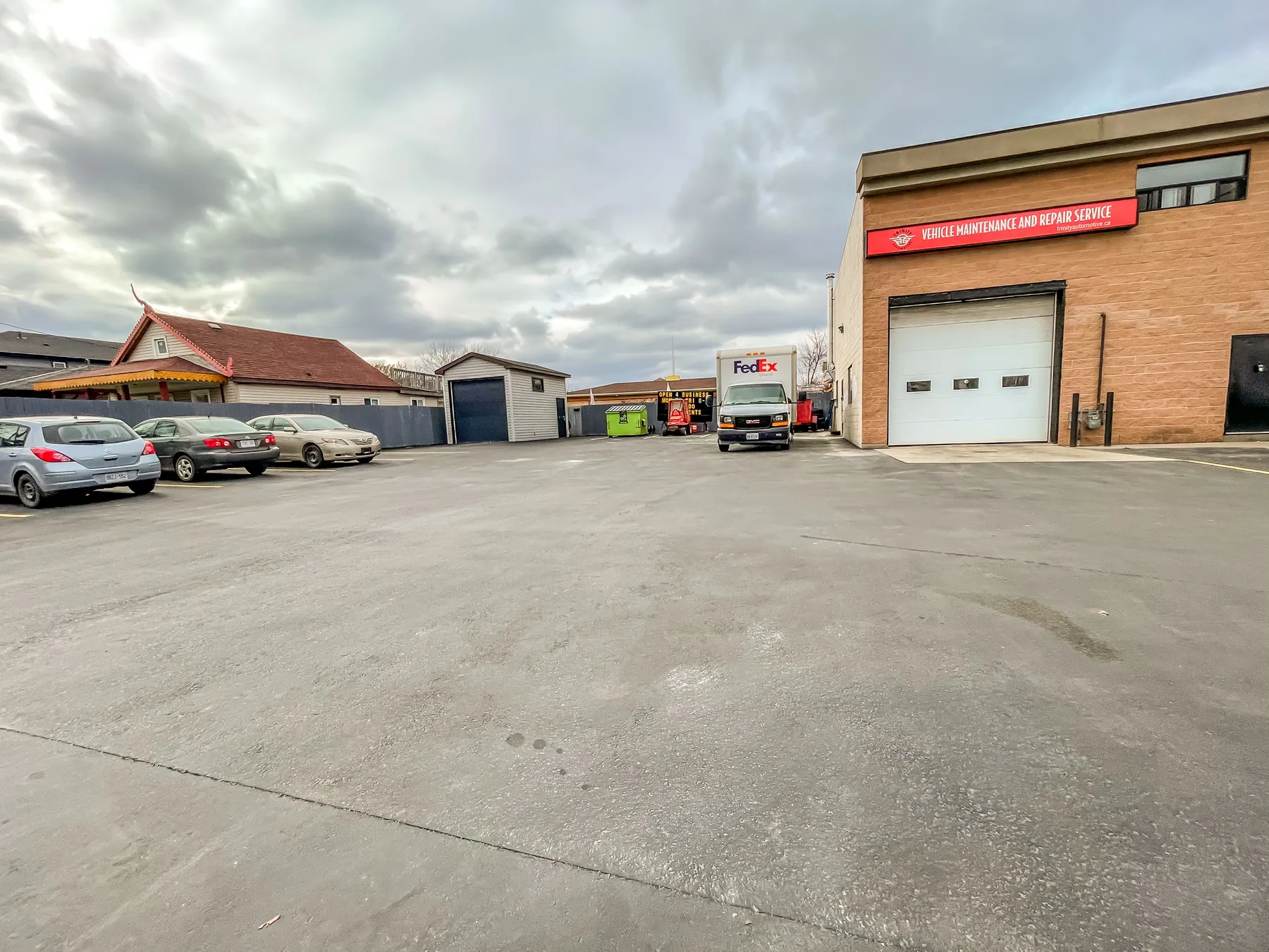 The small rear structure with its roll-up door, the parked vehicles and service building behind it