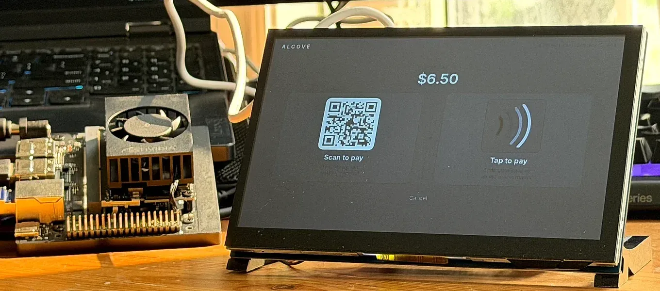 The Alcove bench unit on a workbench beside an NVIDIA edge board, its touchscreen showing a $6.50 checkout